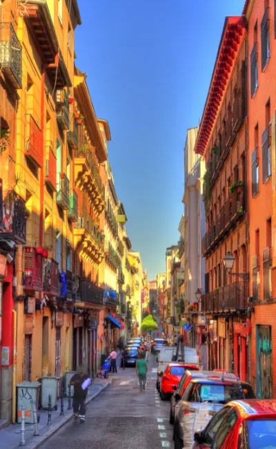 A quaint narrow street in Madrid, with cars parked along both sides, ideal for a solo travel adventure.